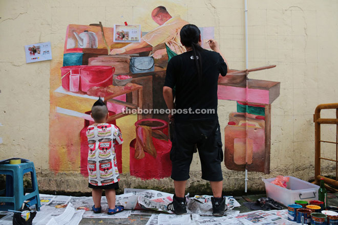 Tiong (right) paints on the wall while a boy looks on.